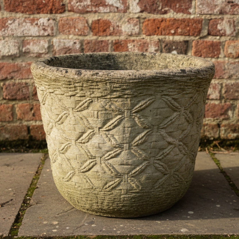 Ornate concrete planter with geometric pattern against a brick wall.