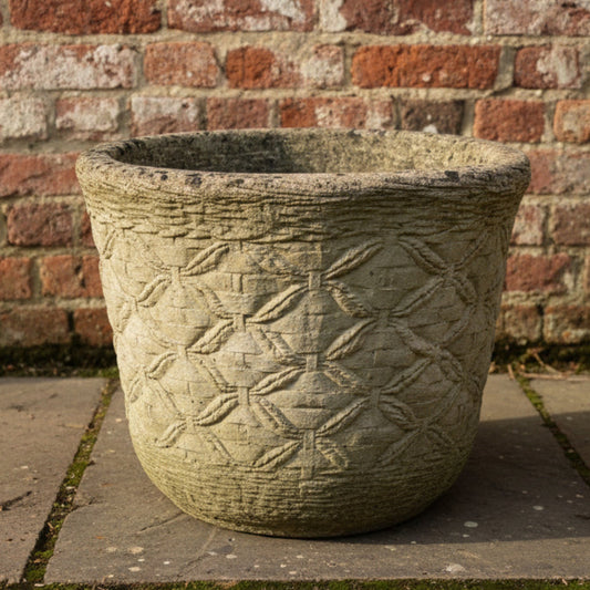 Ornate concrete planter with geometric pattern against a brick wall.