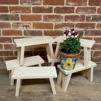 small wooden stools stacked on a floor with a red brick wall behind.